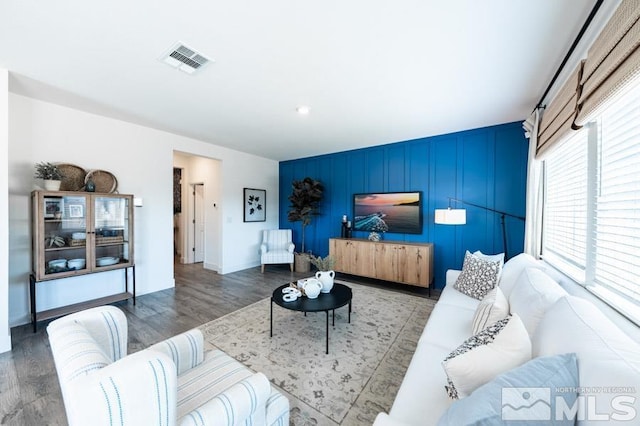 living room featuring visible vents, an accent wall, baseboards, and wood finished floors