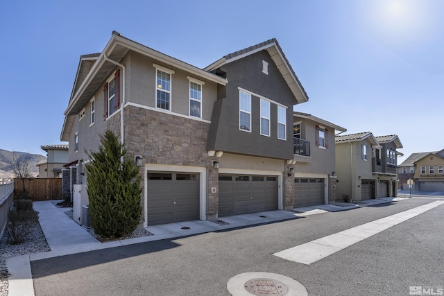 multi unit property featuring fence, an attached garage, stucco siding, stone siding, and a residential view