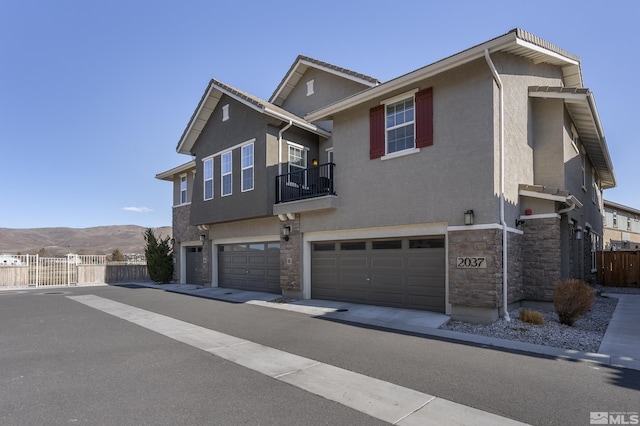 view of front facade featuring fence, stucco siding, a garage, stone siding, and a mountain view