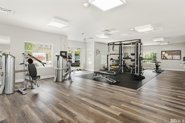 exercise room featuring visible vents, a wall unit AC, baseboards, and wood finished floors