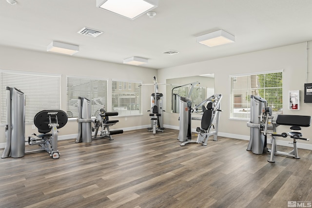 exercise room with wood finished floors, visible vents, and baseboards