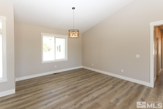 empty room featuring a notable chandelier, lofted ceiling, baseboards, and wood finished floors