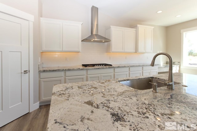 kitchen with a sink, wood finished floors, wall chimney exhaust hood, white cabinets, and stainless steel gas cooktop