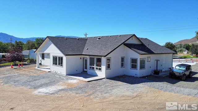 back of property with a mountain view, roof with shingles, and a patio