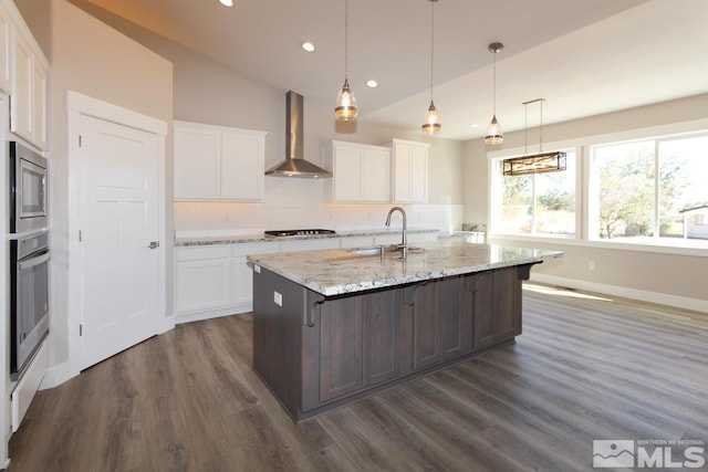 kitchen featuring a sink, tasteful backsplash, stainless steel appliances, white cabinets, and wall chimney range hood