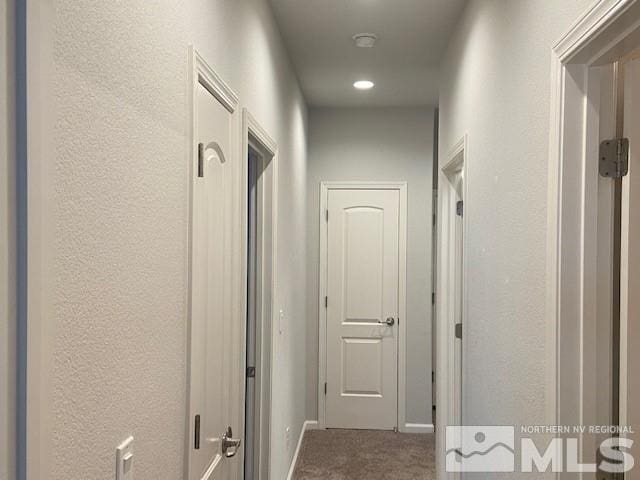 corridor featuring baseboards, carpet, and a textured wall