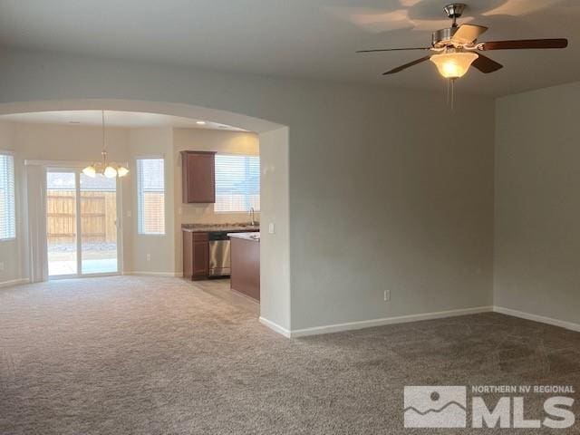 carpeted empty room featuring a sink, ceiling fan with notable chandelier, arched walkways, and baseboards