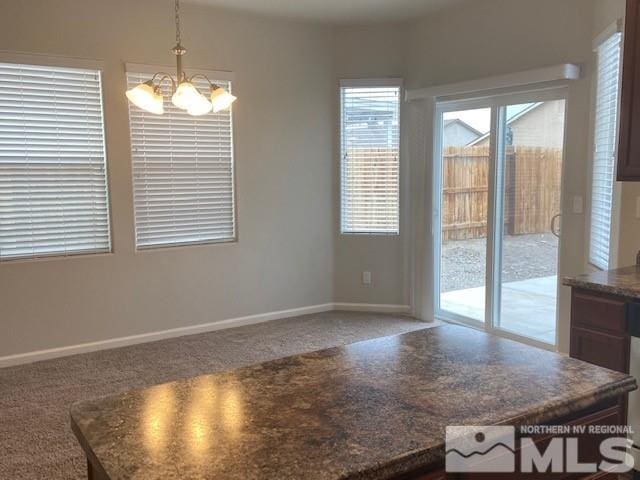 unfurnished dining area featuring baseboards, carpet, and a chandelier