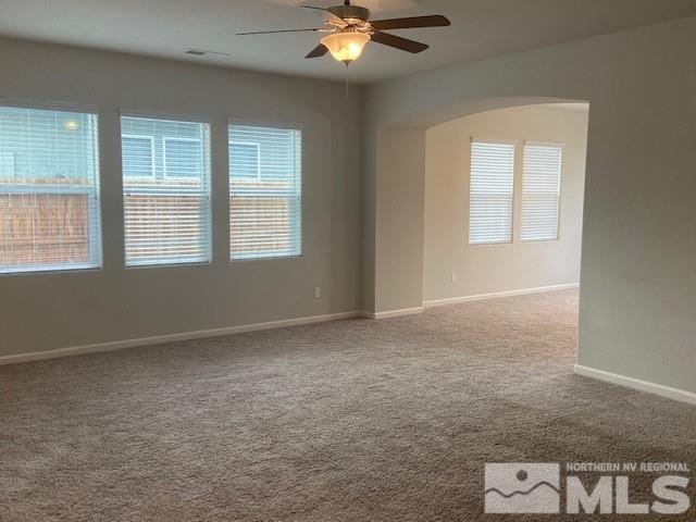 carpeted spare room with baseboards, arched walkways, and ceiling fan