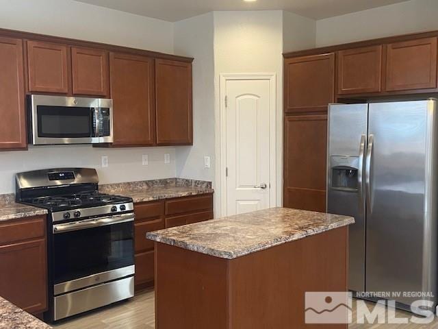 kitchen featuring light wood finished floors, a kitchen island, stone countertops, and stainless steel appliances