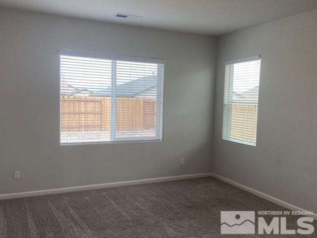 empty room featuring baseboards, visible vents, and dark carpet