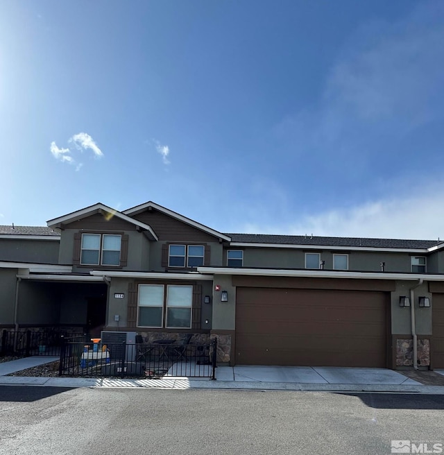 view of front facade featuring a fenced front yard, stucco siding, a garage, stone siding, and driveway