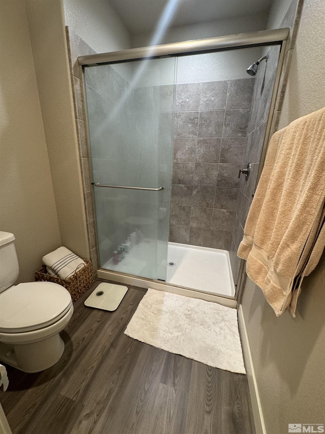 full bath featuring toilet, wood finished floors, and a stall shower