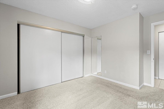 unfurnished bedroom featuring a closet, carpet flooring, a textured ceiling, and baseboards