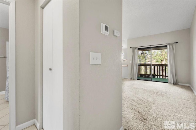 corridor featuring baseboards, light colored carpet, and a textured ceiling