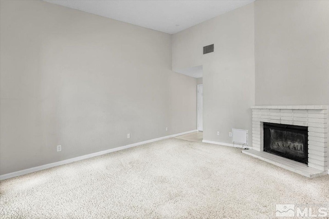 unfurnished living room with visible vents, a brick fireplace, baseboards, carpet floors, and a high ceiling