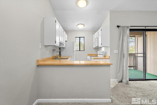 kitchen featuring baseboards, light countertops, white cabinets, white appliances, and a sink