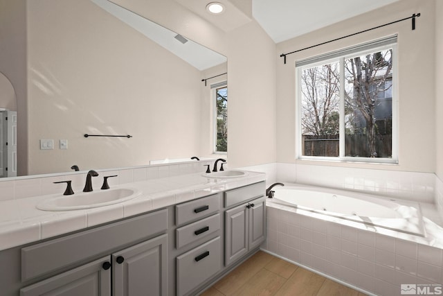 bathroom featuring a sink, a jetted tub, wood finished floors, and double vanity