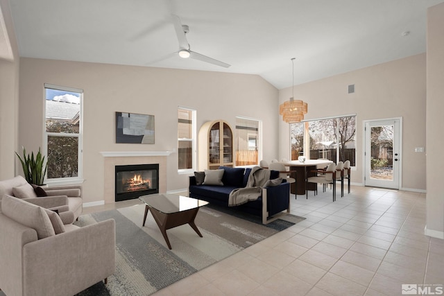 living room with baseboards, a premium fireplace, light tile patterned floors, ceiling fan with notable chandelier, and high vaulted ceiling