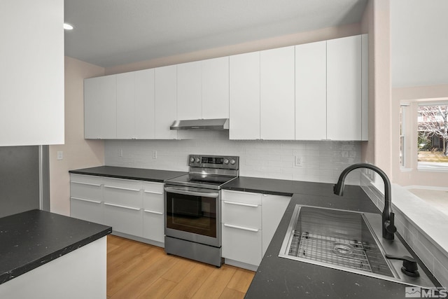 kitchen with under cabinet range hood, light wood-type flooring, dark countertops, and stainless steel range with electric cooktop