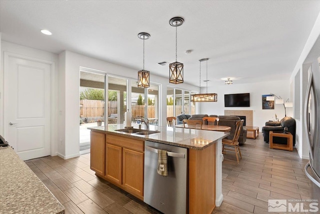 kitchen with a sink, wood finish floors, stainless steel dishwasher, and a kitchen island with sink