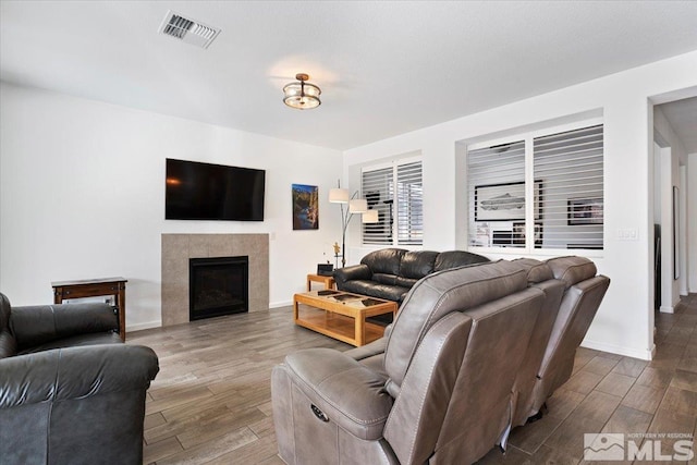 living room with a tiled fireplace, visible vents, baseboards, and wood finished floors