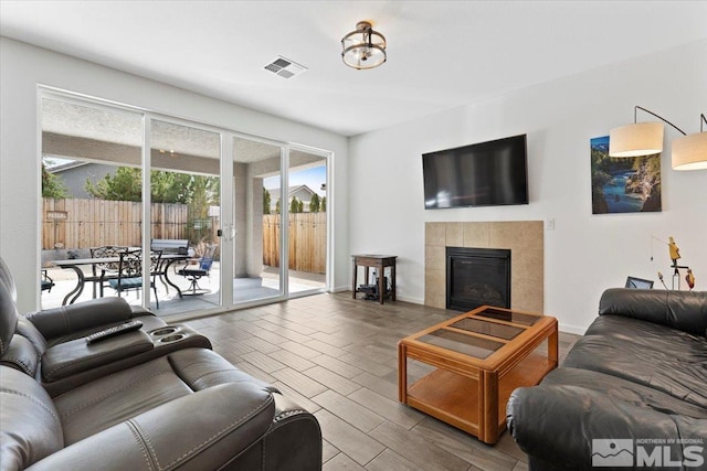 living area featuring a tiled fireplace, baseboards, visible vents, and wood finish floors