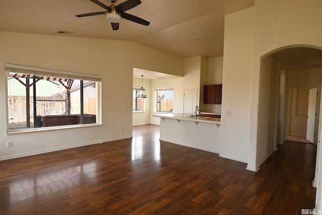 unfurnished living room featuring a ceiling fan, visible vents, dark wood finished floors, arched walkways, and a sink