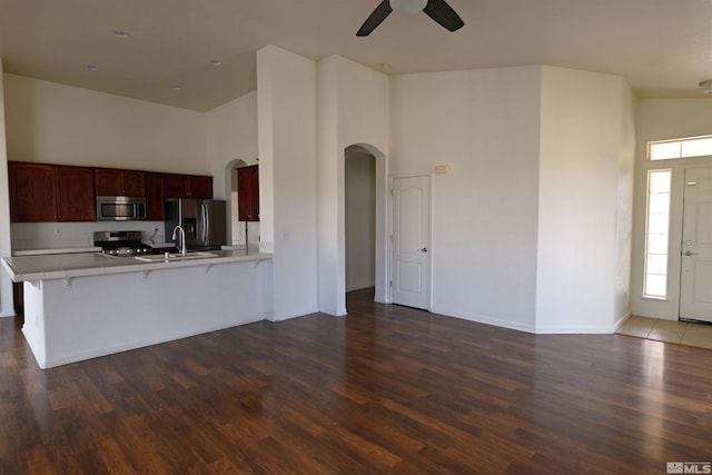 kitchen featuring ceiling fan, light countertops, a towering ceiling, arched walkways, and stainless steel appliances