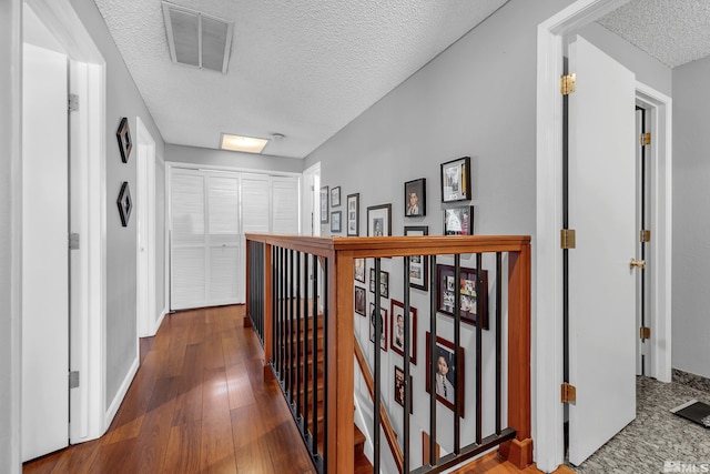 hallway with an upstairs landing, visible vents, a textured ceiling, and wood-type flooring