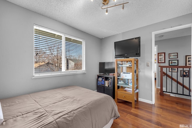 bedroom with wood finished floors, baseboards, and a textured ceiling