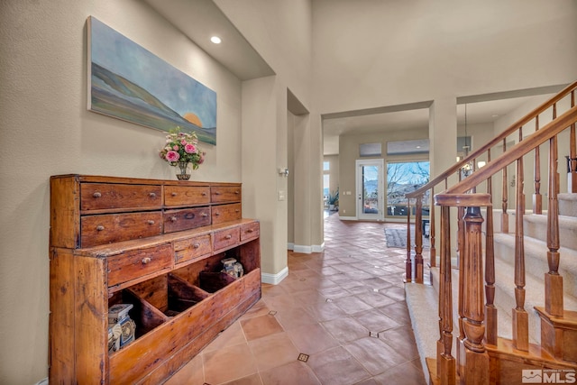 foyer featuring light tile patterned flooring, stairway, baseboards, and a towering ceiling