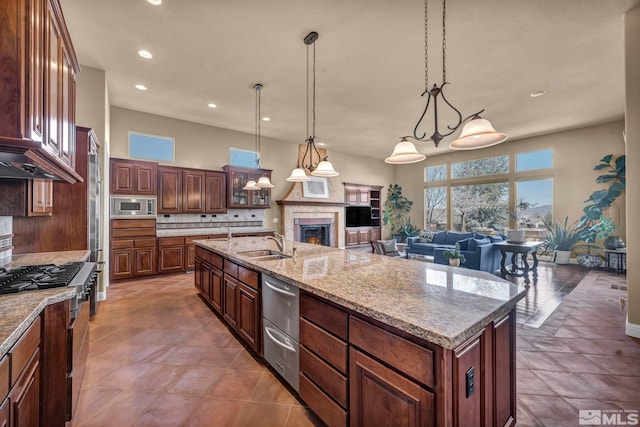 kitchen with a warm lit fireplace, a sink, open floor plan, appliances with stainless steel finishes, and tasteful backsplash