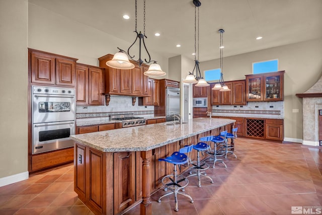 kitchen featuring brown cabinetry, a breakfast bar, a large island with sink, built in appliances, and tasteful backsplash