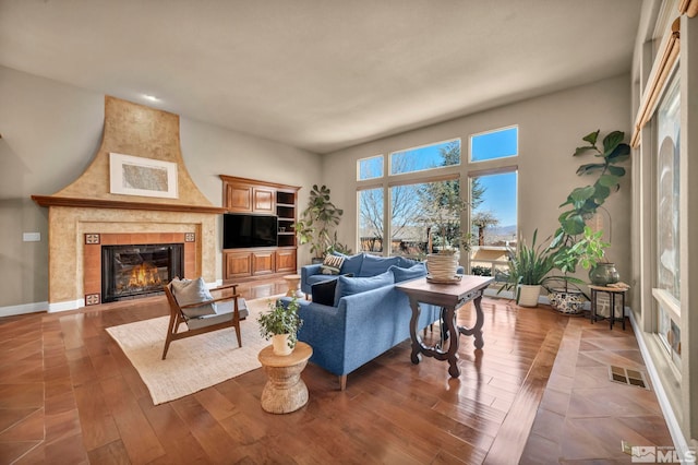 living room featuring a tiled fireplace, visible vents, baseboards, and wood finished floors