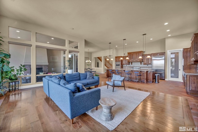 living room with a glass covered fireplace, recessed lighting, a towering ceiling, a notable chandelier, and wood-type flooring