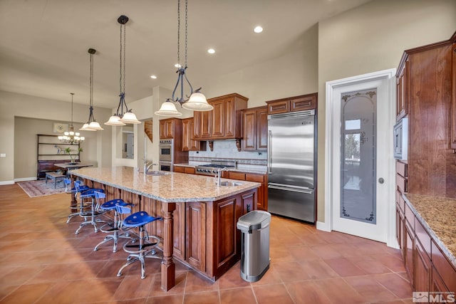 kitchen featuring a breakfast bar, light stone counters, a spacious island, backsplash, and built in appliances