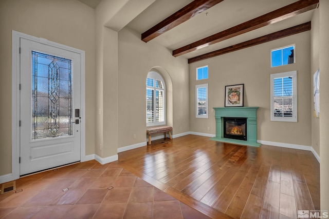 entryway featuring a glass covered fireplace, beamed ceiling, baseboards, and wood finished floors