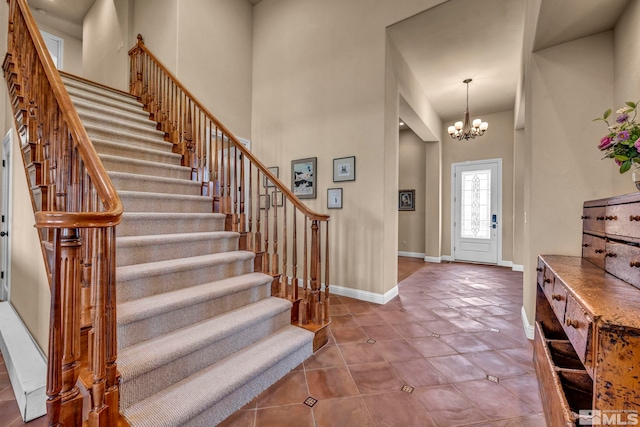 tiled entryway featuring an inviting chandelier, stairway, baseboards, and a high ceiling