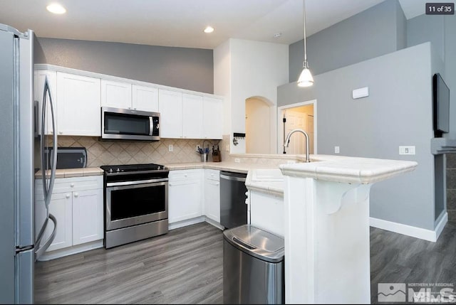 kitchen with a peninsula, stainless steel appliances, decorative backsplash, white cabinets, and light wood-type flooring