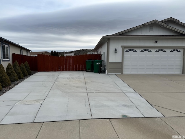 view of side of home featuring concrete driveway, an attached garage, and fence