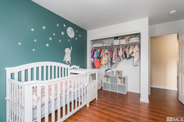 bedroom with a crib, baseboards, a closet, and wood finished floors