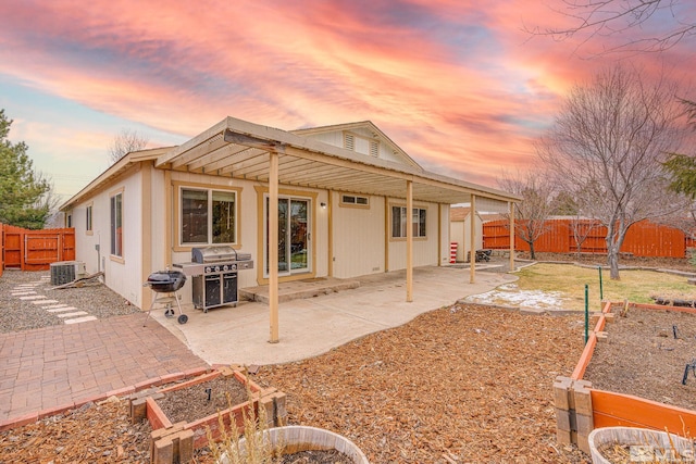 back of house at dusk with a fenced backyard, central AC unit, and a patio