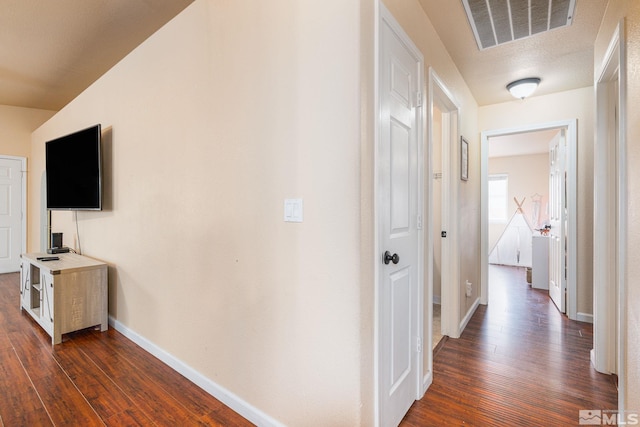 hall featuring dark wood-style floors, visible vents, and baseboards