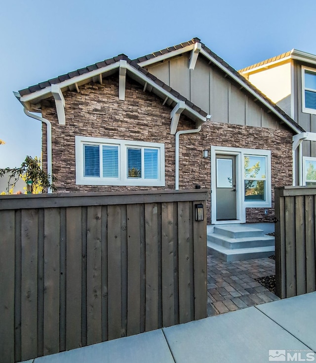 back of property with stone siding, board and batten siding, and fence