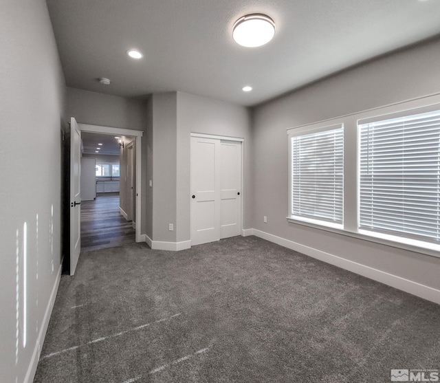 unfurnished bedroom with a closet, recessed lighting, baseboards, and dark colored carpet