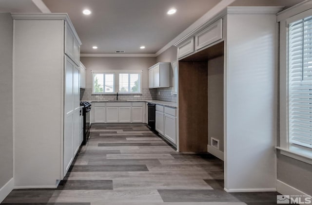 kitchen featuring visible vents, light wood-type flooring, decorative backsplash, black appliances, and a sink