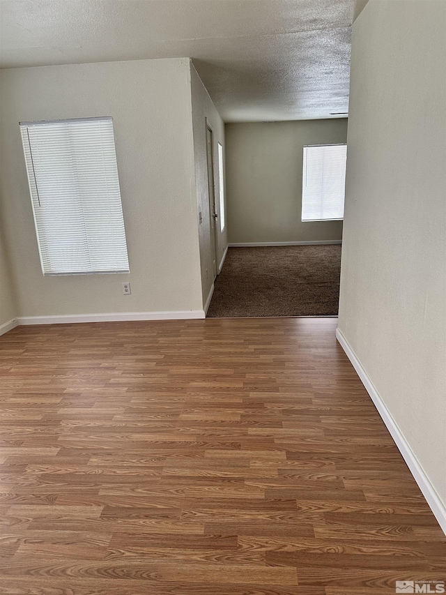 unfurnished room featuring a textured ceiling, baseboards, and wood finished floors