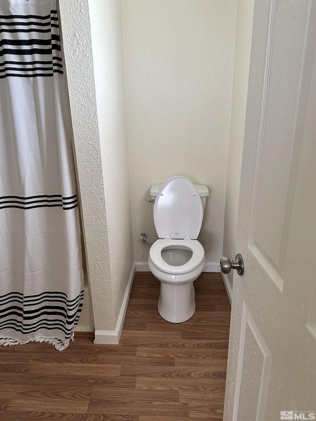 bathroom featuring toilet, curtained shower, wood finished floors, baseboards, and a textured wall