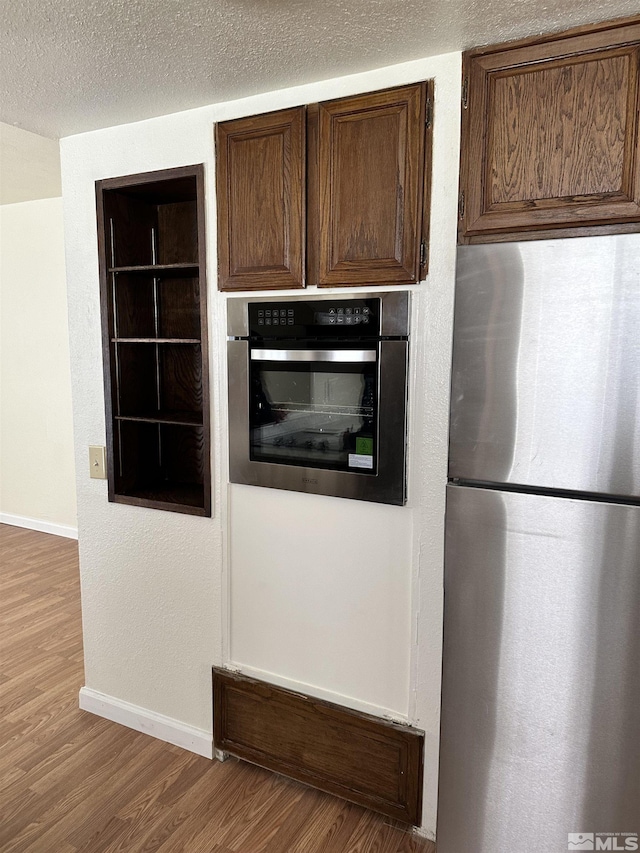 kitchen with wood finished floors, baseboards, dark brown cabinets, appliances with stainless steel finishes, and a textured ceiling
